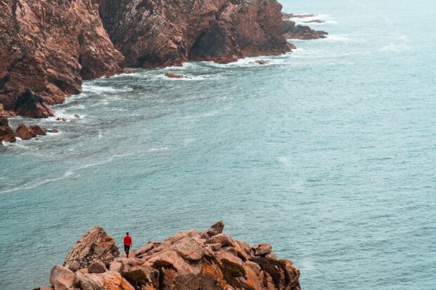 Mann läuft auf Klippe an Steilküste bei Cabo da Roca in Portugal