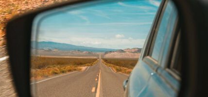 Straße im Rückspiegel auf einem Roadtrip. Im Hintergrund laufen die besten Roadtrip Songs