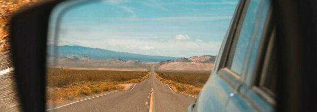 Straße im Rückspiegel auf einem Roadtrip. Im Hintergrund laufen die besten Roadtrip Songs