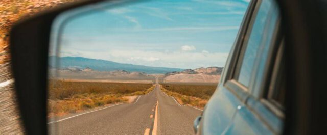 Straße im Rückspiegel auf einem Roadtrip. Im Hintergrund laufen die besten Roadtrip Songs