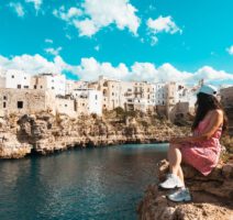 Frau sitzt vor der Küste von Polignano a Mare in Apulien