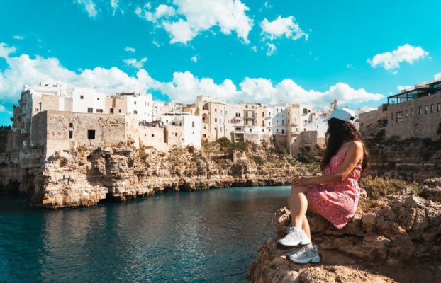 Frau sitzt vor der Küste von Polignano a Mare in Apulien