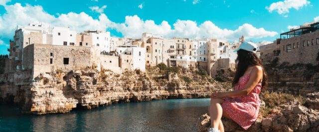 Frau sitzt vor der Küste von Polignano a Mare in Apulien