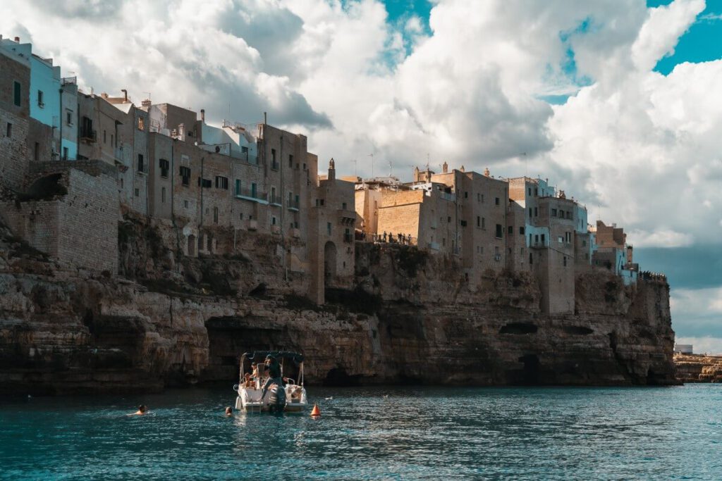 Ein Boot ankert vor der Steilküste von Polignano a Mare und ein paar Touristen schwimmen im Wasser