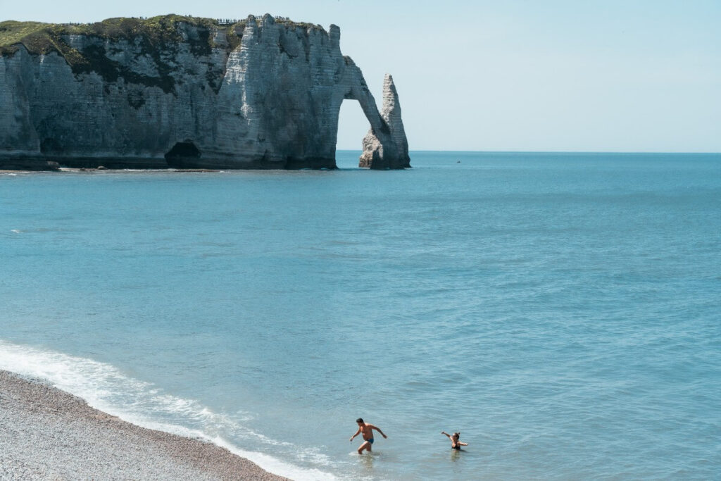 2 Toursiten baden an der Küste vor der markanten Felsformation von Etretat.