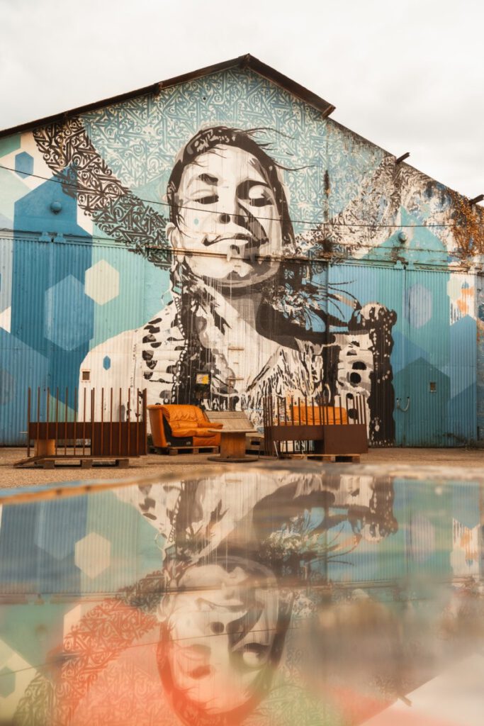 Darwin Ecosystem Bordeaux Grafitti einer Frau auf einer Halle spiegelt sich in einem Tisch