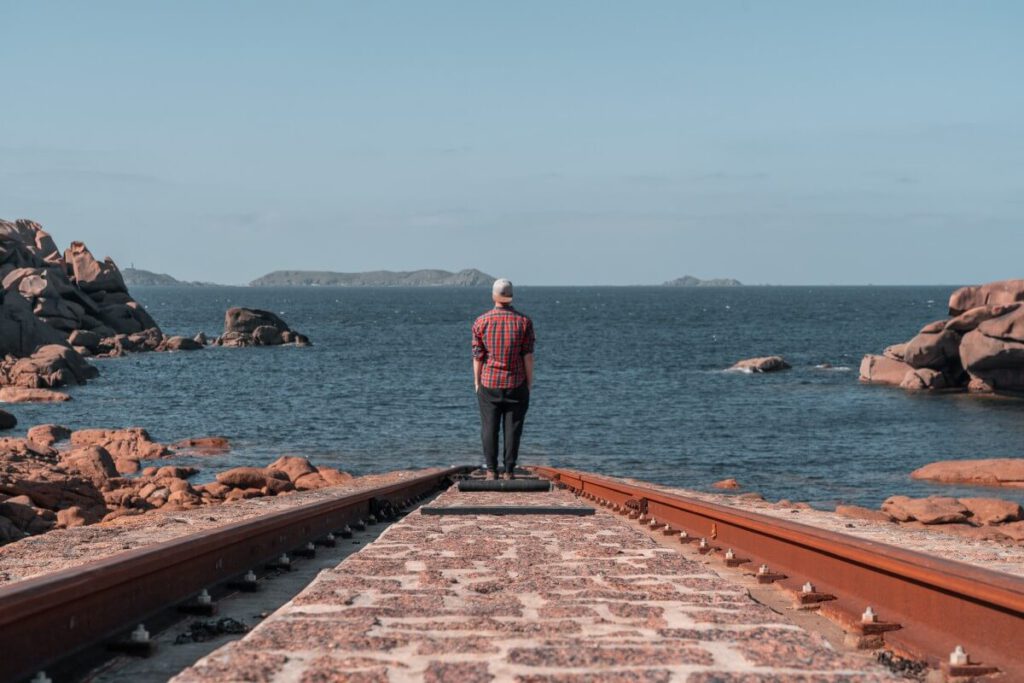 Mann steht an der Küste an einer Schiene an der Côte de Granit Rose 