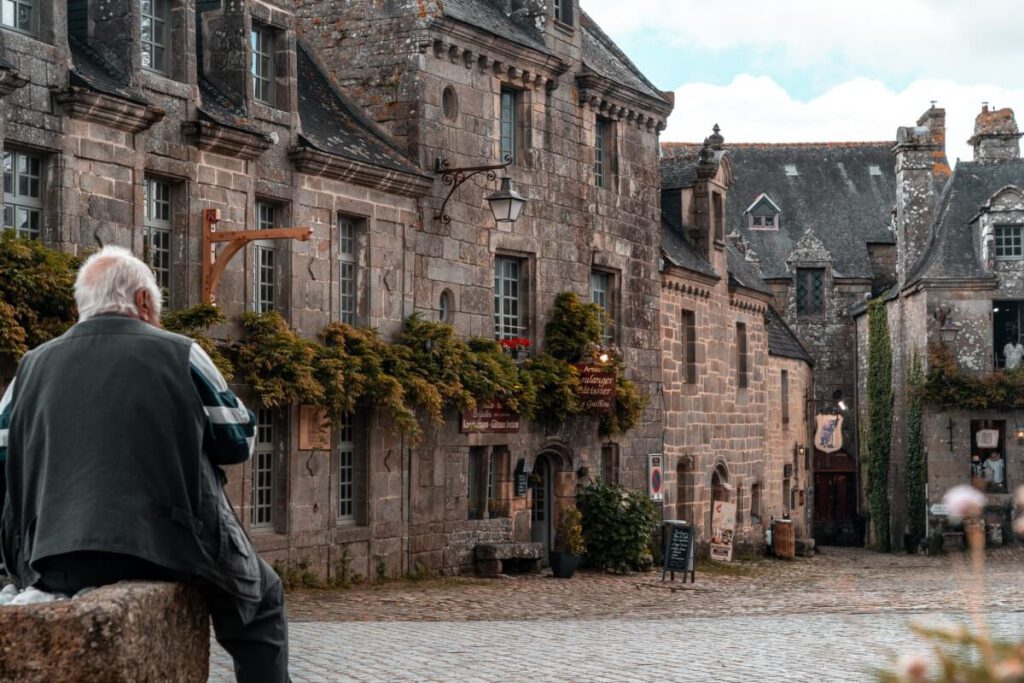 Ein Mann sitzt auf dem Brunnen am Locronan Marktplatz