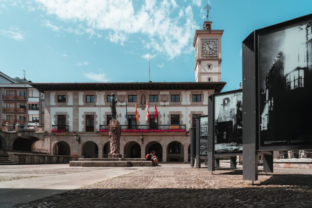 Schilder mit Bildern von Gernikas Bombadierung auf dem dem Foru Plaza mit Blick aufs Rathaus.