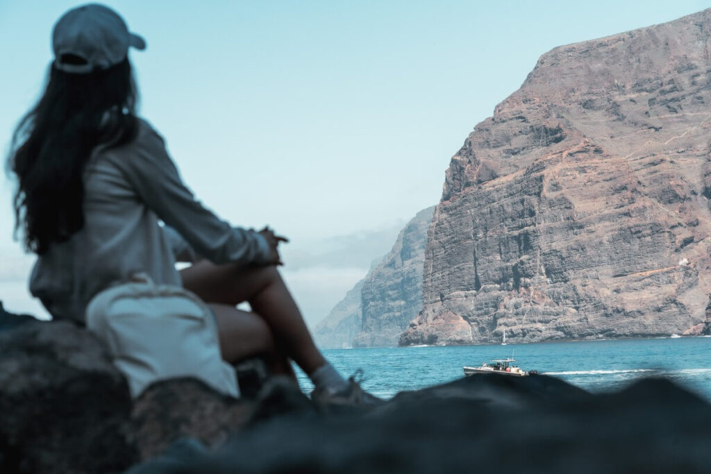 Frau sitzt am Strand und schaut auf die Los Gigantes Klippen